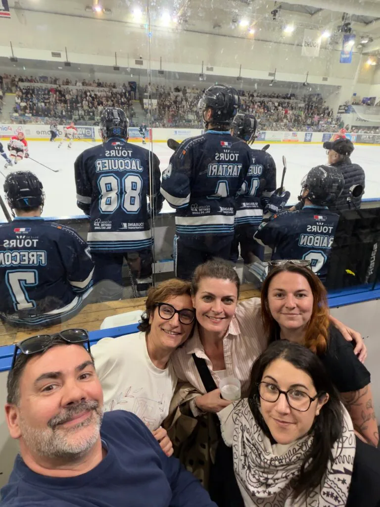 Une soirée d’équipe au cœur du hockey tourangeau Équipe de l’agence réunie à la patinoire de Tours lors d’un match de hockey, avec les joueurs des Remparts visibles en arrière-plan.